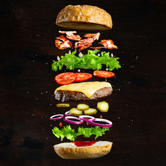 Floating burger isolated on black wooden background. Ingredients of a delicious burger with ground beef patty, lettuce, bacon, onions, tomatoes and cucumbers - obrazy, fototapety, plakaty