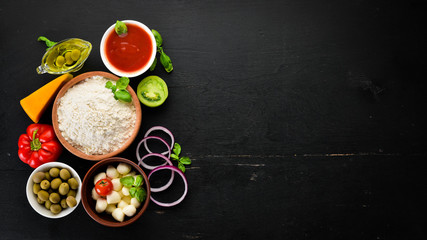 Ingredients for pizza. Mushrooms, sausages, tomatoes, vegetables. Top view. On a black wooden background. Free copy space.