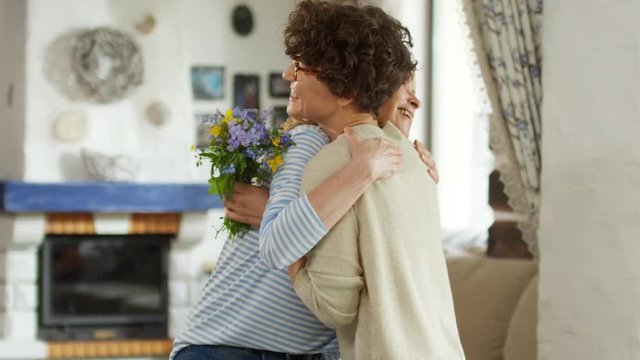 Medium shot of Caucasian woman with short curly hair giving bunch to blond middle-aged woman and hugging her