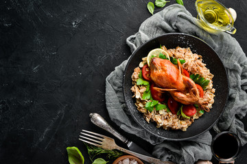Baked quail with oatmeal and vegetables. On a black background. Top view. Free space for your text.