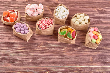 candies, lollipops, caramel, in paper bags on wooden background