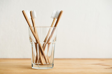 Four bamboo toothbrushes in a glass on a wooden table with copy space