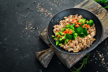A plate of healthy food. Oatmeal with broccoli, carrots and parsley. Top view. On a black background. Free copy space.
