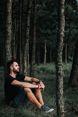 Young depressed man sitting alone in the forest