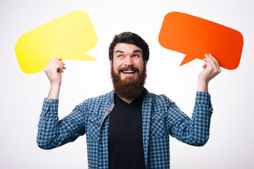 Young handsome bearded man holding blank paper speech bubble in hands with copy space for text. Bearded male, wearing hipster checkered shirt with empty message box. Isolated, background.