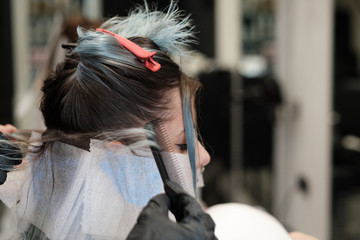 Una mujer recibe el tinte en una peluquería y se ven las manos de la peluquera