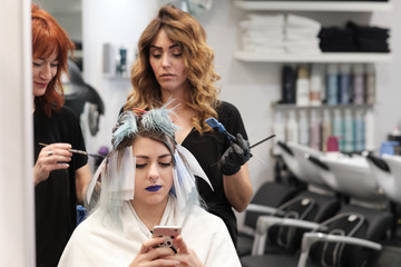 Una chica chatea con el móvil mientras dos peluqueras le ponen el tinte