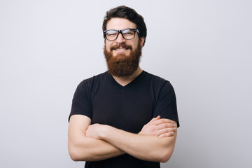 Portrait of a smiling bearded in glasses man standing with arms folded adn looking at camera