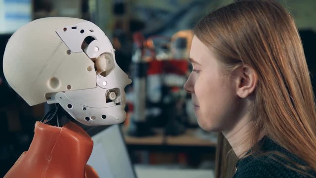 Female engineer looks at a droid working, side view.