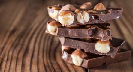 Stack of pieces of chocolate with whole nuts on wooden table.