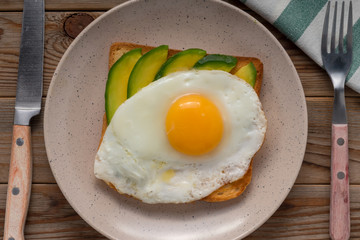 Toast bread with fried eggs, avocado. And cucumber slices on wooden table. Top view. Closeup