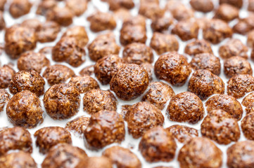 Chocolate cereal balls in milk as food background.