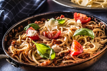 Italian pasta spaghetti bolognese in old pan with tomatoes parmesan cheese and basil