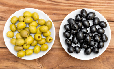Saucers with black and green olives on wooden table. Top view.