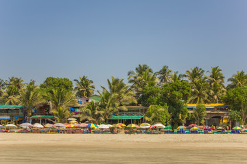 view of the colorful beach umbrellas with sun beds against the backdrop of restaurants and green...