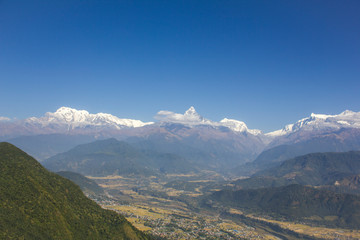 Fototapeta premium city in a green mountain valley on the background of the Annapurna snow ridge under a clear blue sky