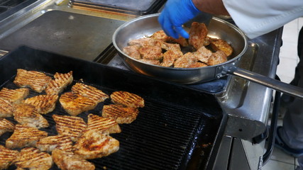 The process of cooking in the restaurant's kitchen, the chef in blue gloves frying meat in a pan and grilling in the professional kitchen of the restaurant