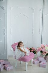 young beautiful girl ballerina in a white pink dress is standing in a white room near a white table is holding a bouquet of flowers.