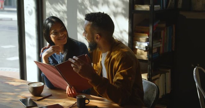 Front view of young Asian couple discussing over menu card in cafe 4k