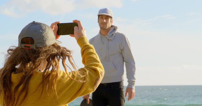 Rear view of young caucasian woman clicking photo of young caucasian man with camera on the beach 4k