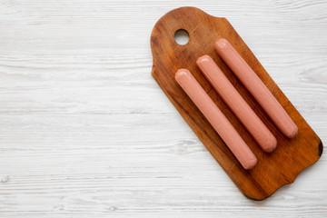Hot dog sausages on rustic wooden board over white wooden background, top view. Flat lay, overhead, from above. Copy space.