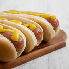 Hot dog with yellow mustard on rustic wooden board on white wooden table, side view. Close-up.