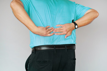 Close-up caucasian man with pain in kidneys isolated on a gray background. Man with back ache clasping her hand to her lower back. Man suffering from ribbing pain, waist pain.