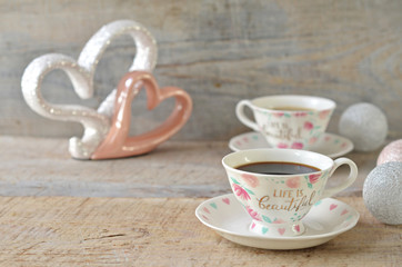 A cup of coffee on a bright wooden background. Porcelain hearts in the background