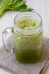 Green celery smoothie in glass jar over white wooden background, side view. Close-up.