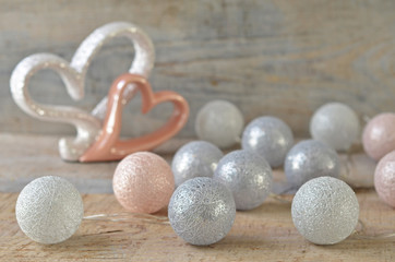 Cotton ball lights on a wooden background. Silver and pink hearts on the background
