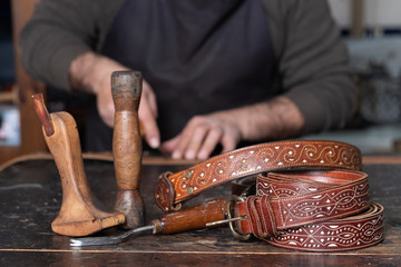 leather belts with leather tools on table and craftsman working behind