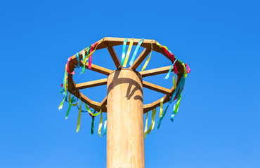 Wooden wheel with colorful ribbons on blue sky background