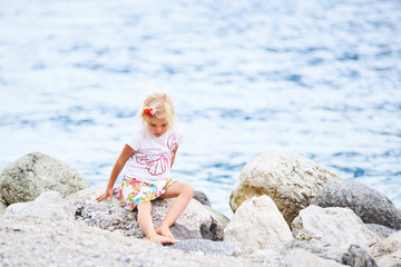 Fototapeta na wymiar A little blond girl posing on the beach at the lake Lago di garda, Limone, Italy
