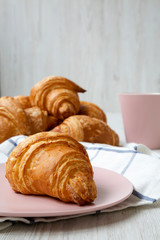 Homemade golden croissants and cup of coffee over white wooden background, side view. Selective focus.