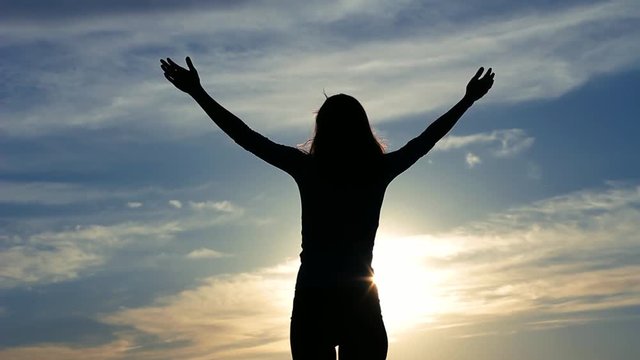Silhouette young woman outstretching arms against beautiful sky and sun