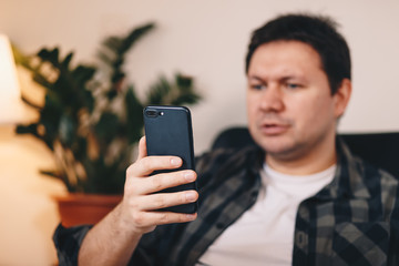 Close up of a man having a video call with his friends over a smartphone, while sitting in a personal working space at home.