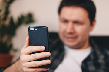 Close up detail of a young man's hand holding a mobile phone, taking a selfie, while sitting in a personal working space at home. Focus on the device.