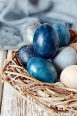 Dyed Easter vintage eggs with scuffs on a light gray background in a wicker basket. Stylish...