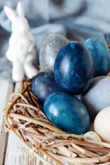 Dyed Easter vintage eggs with scuffs on a light gray background in a wicker basket. Stylish...