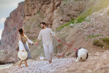 A young couple in love walks with a big dog on the beach in summer or spring