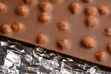 Bar of chocolate with a lot of nuts lays on foil