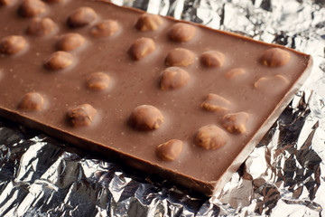 Bar of tasty milk chocolate with nuts lays on foil