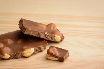 Broken bar of chocolate and nuts on wooden background