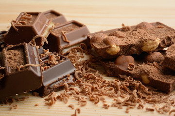 Broken bar of milk chocolate with nuts seasoned with cocoa powder and grind chocolate lays on wooden table