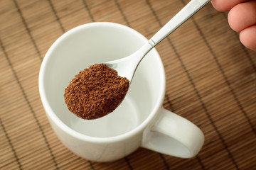 Spoon with instant coffee in a man`s hand over the empty cup. Making coffee
