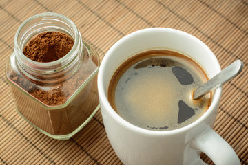 Coffee in white cup and jar of coffee on the brown bamboo background