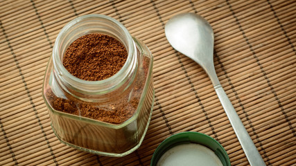 Obraz na płótnie Canvas Jar of coffee with cover and a spoon on a brown bamboo background