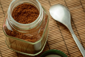 Glass jar of coffee on a brown background with cover and coffee spoon