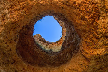 Famous caves in a beach rock formation in the Algarve, Portugal. Through the hole in the ceiling of the cave you can see the blue sky