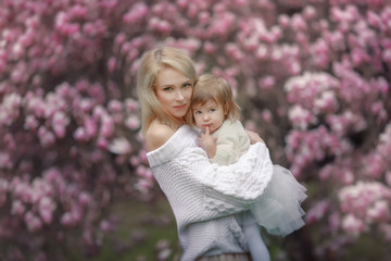 Portrait of happy joyful child in white clothes over tree flowers blossom background. Family playing together outside. Mom cheerfully hold little daughter Newborn spring concept